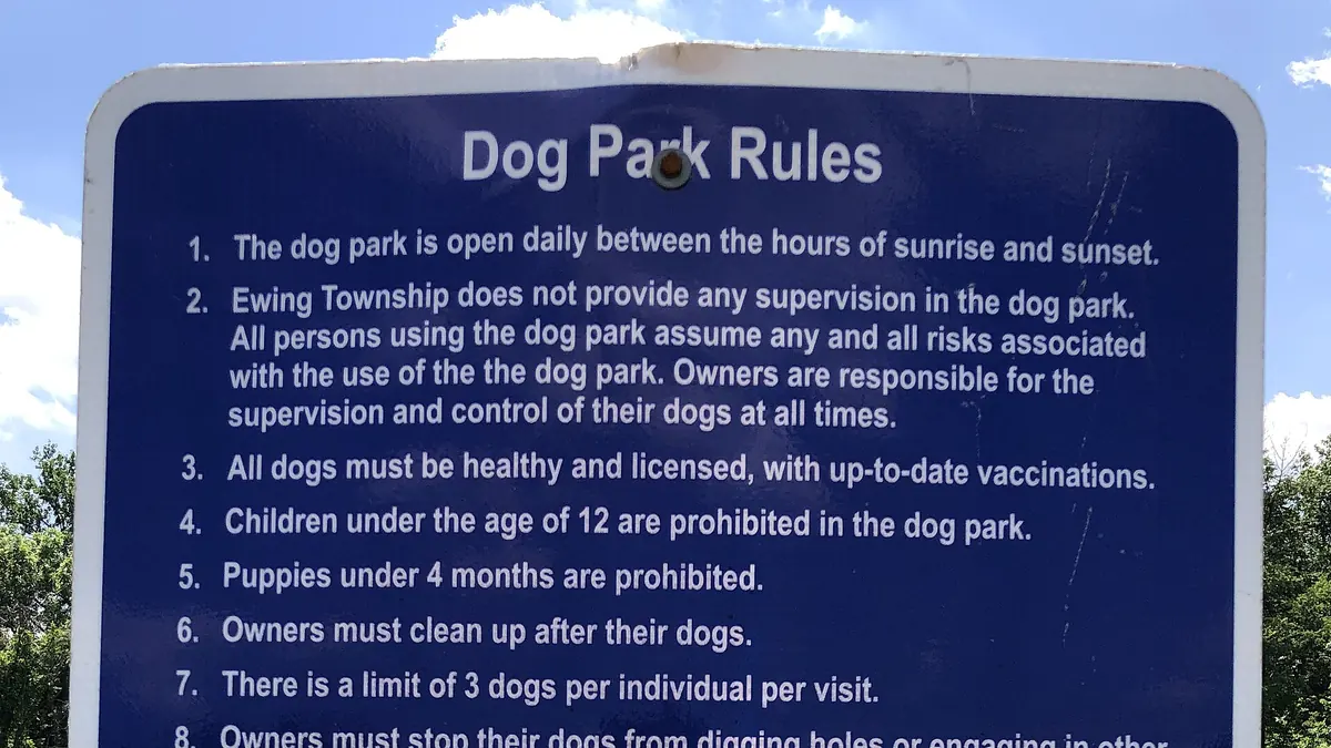 A posted list of dog park rules on a sign by a fence